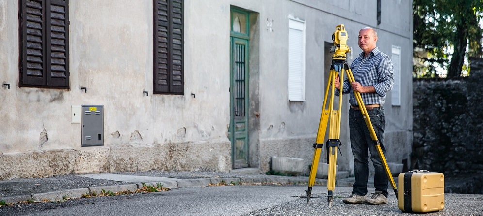 surveyor using total station next to a row of houses